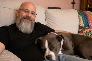 Bald white man with a long gray beard and a pit bull in his lap